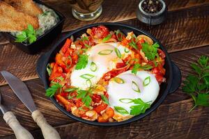 Shakshuka with grilled bread. Fried eggs with tomato, pepper, garlic and herbs photo