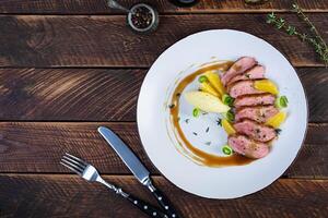 Roast duck fillet with mashed potato and orange sauce on wooden background photo