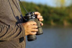 Asian man uses binoculars to observe local birds along a river. Soft and selective focus. photo