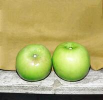 two green apples sit on a wooden shelf photo