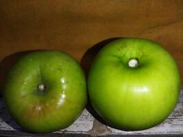 two green apples sit on a wooden shelf photo