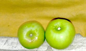 two green apples sit on a wooden shelf photo