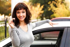 Happy owner of a new car, smiling cute young girl showing a key photo