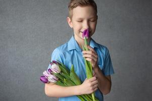 Cute boy closed his eyes and holds a bouquet of colorful tulips and smells the flower. photo