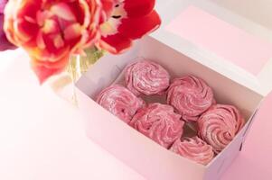 Pink marshmallow lies in a gift box near a vase with tulips on a pink background photo