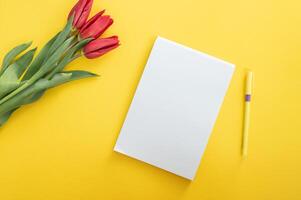 Top view of yellow desk with blank notebooks mockup with pencil and tulips. notebook photo