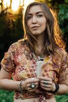 Beautiful young woman wearing bohostyle clothes posing in the rays of the evening sun, sunset. Boho style fashion, female wearing silver jewelry having fun in park outdoors. photo