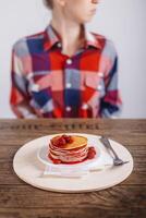 American Pancakes with raspberry jam on a wooden table, woman in the background, food advertising concept. Closeup, selected focus. photo