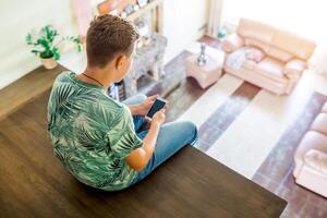 The teenager is using cell phone, sitting on the second floor of the house. Top view of the room. Selective focus. photo