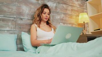 Kaukasisch vrouw in pyjama lezing een online artikel Aan haar laptop terwijl resting in de bed video