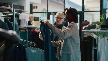 africano americano Al dettaglio impiegato mostrando nuovo moda collezione per anziano cliente nel Dipartimento memorizzare a il centro commerciale. incinta assistente fabbricazione colore suggerimenti per regolare cliente, consumismo. telecamera b. video