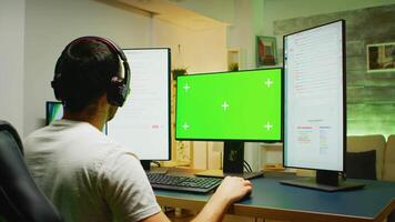 Back shot of young man in a room with neon light playing on computer with green screen. video