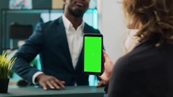 Store manager holding smartphone with greenscreen layout at cash register, working on commercial activity with clients. Woman retail clerk using chromakey display and isolated mockup. Camera A. video