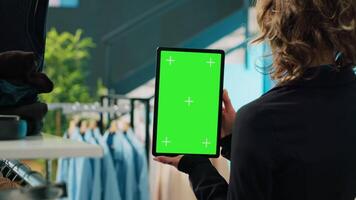 femme vente au détail assistant en portant tablette avec écran vert afficher montré dans département magasin, en utilisant chromakey modèle tandis que vente mode articles. employé travail à couper centre. caméra un. video