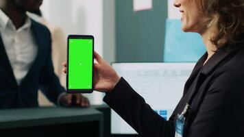 Mall employee showing greenscreen layout on phone at checkout counter, working in fashion industry and selling clothing. Assistant looking at mobile device display with mockup template. Camera A. video