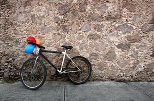 Old bicycle with colorful balloons resting on old rock wall in Mexico, with space for text photo