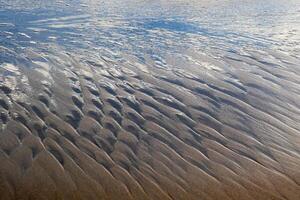 Background of waves in the sand generated by sea waves and sun shine photo