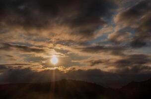 Sunset with sun rays between the clouds, mystical scene with space for text photo