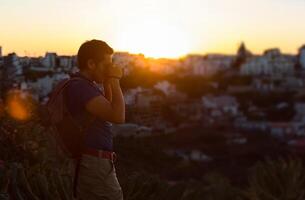 joven hombre tomando un foto con su cámara a puesta de sol