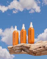 Three orange cosmetic spray bottles laying on logs, sky background. Clipping path of each element included. 3D rendering illustration. photo