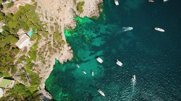 Coastal Aerial Landscape with Boats and Rocky Cliffs in summer lush greenery. Iconic sea stacks Faraglioni emerge from azure waters of Capri, Italy. video
