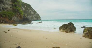 Secluded beach with azure waters. A serene sand shore by steep cliffs and clear, turquoise ocean waves. video