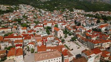 Makarska town in Croatia. City embraced by the towering grace of Biokovo mountain. The central square, aerial view of red roofs. video