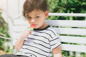 cute latin indian kid child eating sweet fruit ice cream sitting outdoor colorful lovely. photo