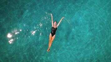 heiter schwimmen im Türkis Gewässer. ein Person schwebend friedlich im klar Meer, Antenne oben Nieder Aussicht von Frau schwebend im Ozean. video