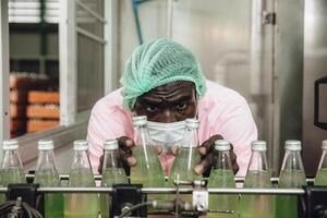 African Nigerian staff worker work in drink factory quality check at conveyor belt product line photo