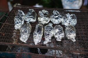 fish or potato wrapped covering with aluminium foil paper grilling on charcoal stove photo