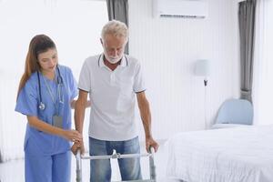 Physical therapist nurse supporting patient elderly senior old man practicing leg muscle recovery with walker equipment photo