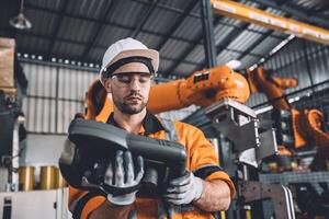 Engineer team service robot welding working in automation factory. Male worker operate robotic arm software hand controller in automated manufacturing industry technology. photo