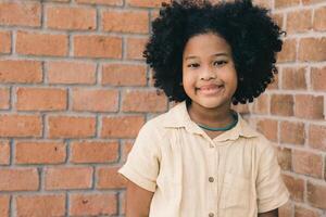 cute black African healthy child girl standing happy smile with copy space brick wall in school. photo