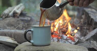 koffie is gegoten in een mok van een koffie maker. ontbijt in de buurt de brand in de toerist kamp. reizen concept. 4k video