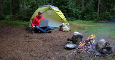 uma homem trabalho em uma computador portátil dentro uma turista acampamento dentro uma lindo floresta. conceito do freelancer, digital nômade ou controlo remoto escritório. 4k video