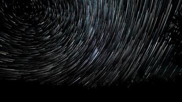 Star trails in the night sky. Stars move around a polar star. Silhouettes of trees photo