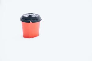 Hot coffee in a red paper cup on the snow outside during a snowfall, close-up photo