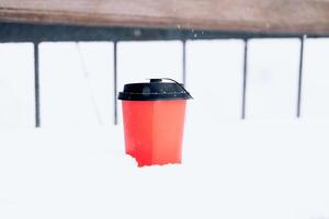 Hot coffee in a red paper cup on the snow outside during a snowfall, close-up photo