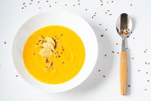 pumpkin cream soup with sesame seeds on a white background. Yellow vegetable soup with spoon photo