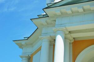 Part of the roof of an ancient house and facade with yellow walls and white columns. Architecture of the restored section of the building. photo