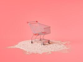 Shopping Cart on Pile of Sand Against Coral Pink Background photo