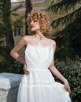 A woman in a white dress stands in front of a house. photo