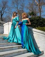 Two women in blue dresses stand in front of a staircase. photo