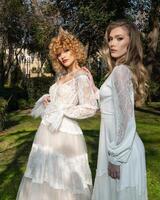 Two women in a white wedding dress stand in a park photo