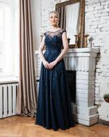 A woman in a blue dress stands in front of a fireplace photo