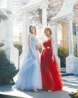 Two women in red dresses stand in front of a white columns. photo