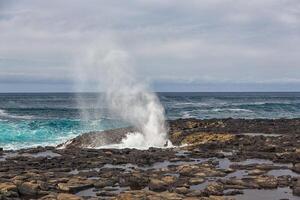 Turbulent ocean waves with white foam beat coastal stones photo