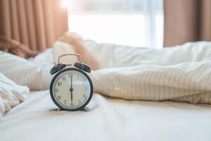 alarma reloj con asiático mujer en cama mientras durmiendo, joven adulto hembra despertar arriba tarde en el temprano Mañana. relajante , somnoliento, diario rutina y tener un bonito día conceptos foto