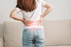 woman having back body ache during sitting on Couch at home. adult female with muscle pain due to Piriformis Syndrome, Low Back Pain and Spinal Compression. Office syndrome and medical concept photo